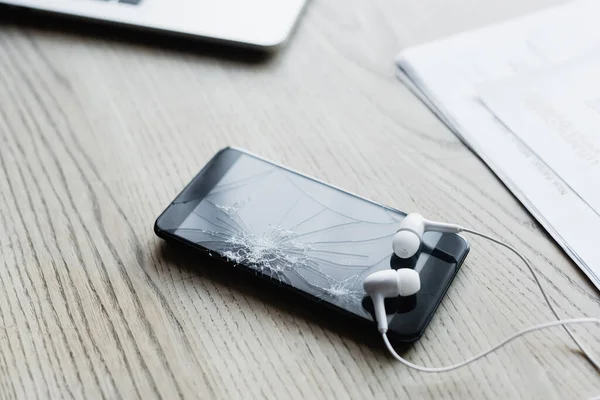 Vista cercana de auriculares con teléfono inteligente roto sobre fondo de madera texturizada - foto de stock