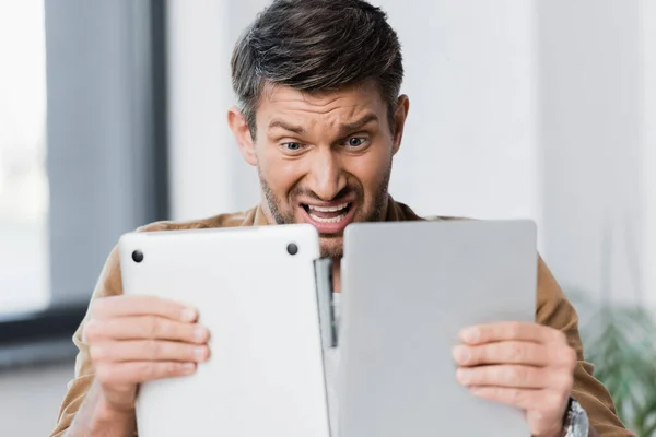 Scared businessman looking at broken laptop on blurred background — Stock Photo