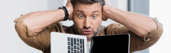 Homme d'affaires fou avec les mains près de la tête regardant ordinateur portable cassé sur fond flou, bannière — Photo de stock