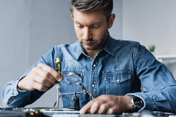 Riparatore mirato con cacciavite che fissa il telefono cellulare sul posto di lavoro in primo piano sfocato — Foto stock