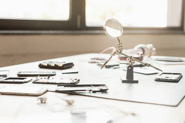 Pièces démontées de téléphones mobiles avec loupe sur la table avec fenêtre floue sur le fond — Photo de stock