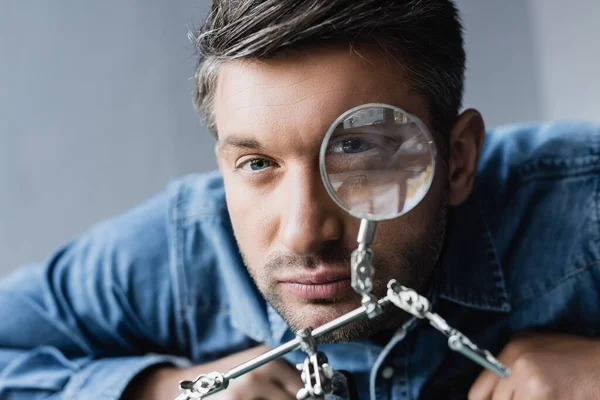 Portrait of repairman looking at camera through magnifier on blurred background — Stock Photo