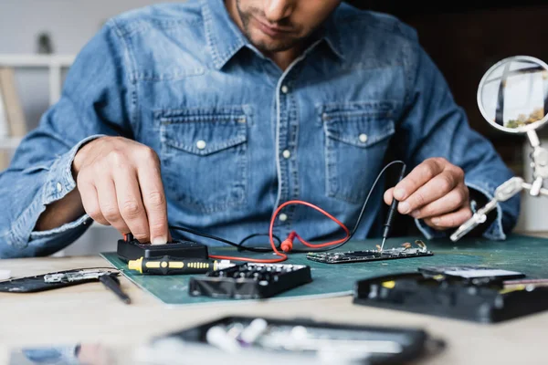 Cropped view of repairman using multimeter while holding sensor on disassembled part of mobile phone on blurred foreground — Stock Photo