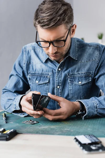 Focused repairman disassembling broken smartphone on workplace on blurred foreground — Stock Photo