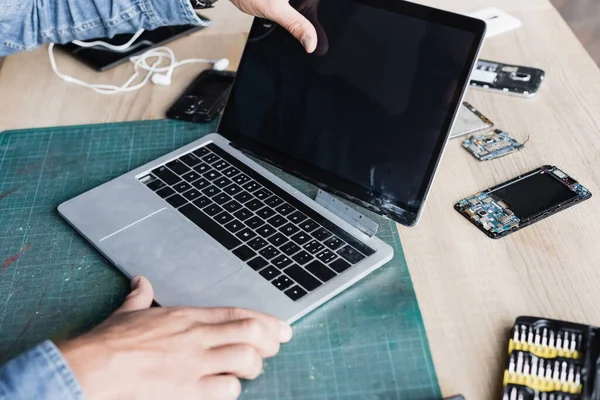 Ausgeschnittene Ansicht des Reparateurs mit beschädigtem Laptop mit leerem Bildschirm am Arbeitsplatz mit zerlegten Teilen von Mobiltelefonen — Stockfoto