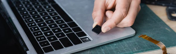 Cropped view of repairman holding broken key of keyboard near laptop at workplace, banner — Stock Photo