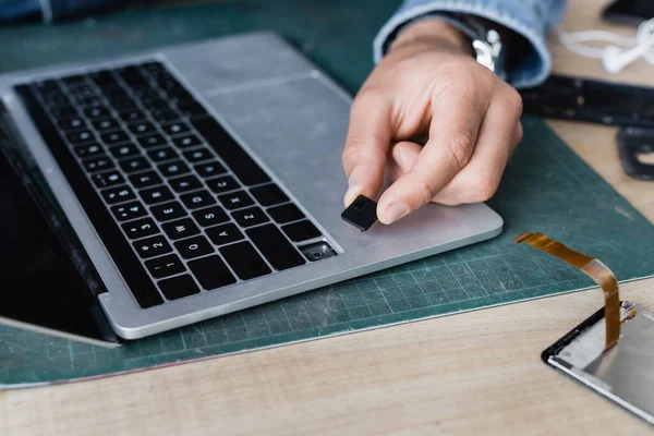 Cropped view of repairman holding broken key of laptop keyboard at workplace on blurred background — Stock Photo