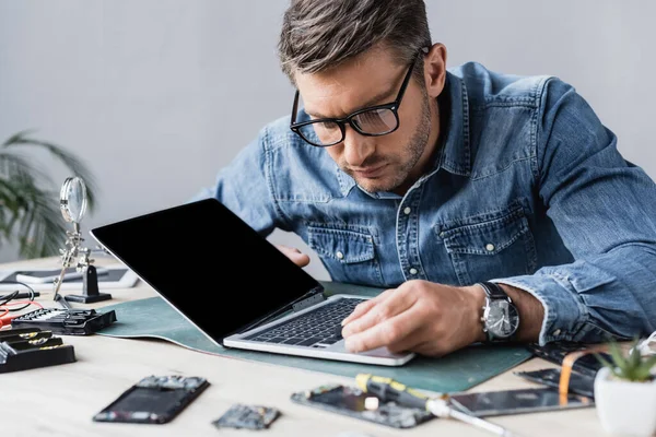 Riparatore focalizzato con tasto rotto guardando la tastiera del computer portatile danneggiato sul posto di lavoro in primo piano sfocato — Foto stock