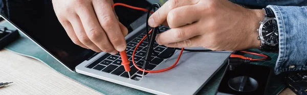 Vista cortada do reparador segurando sensores de multímetro no teclado quebrado do laptop no local de trabalho, banner — Fotografia de Stock