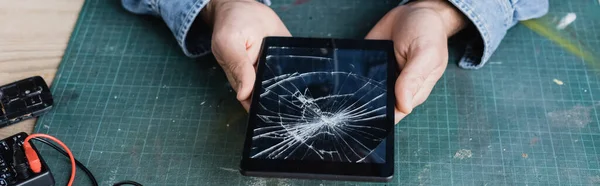 Cropped view of repairman holding smashed digital tablet at workplace, banner — Stock Photo