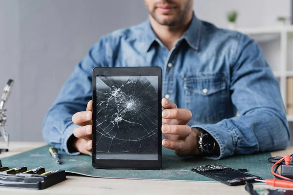 Cropped view of repairman showing smashed digital tablet, while sitting at workplace — Stock Photo