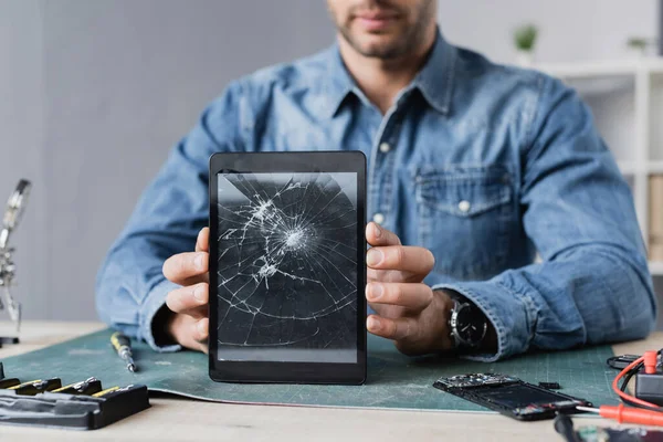 Vue recadrée du réparateur montrant une tablette numérique fracassée, assis sur le lieu de travail — Photo de stock