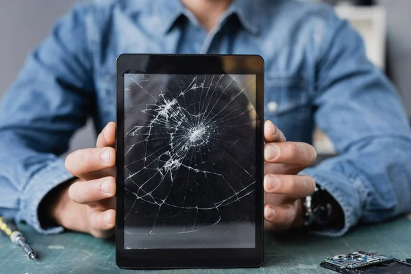 Vista de cerca de la tableta digital aplastada en manos del reparador en el lugar de trabajo sobre un fondo borroso - foto de stock