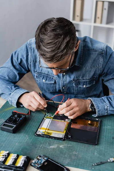 Reparador con sensores de retención de multímetro en parte rota de la tableta digital en el lugar de trabajo - foto de stock