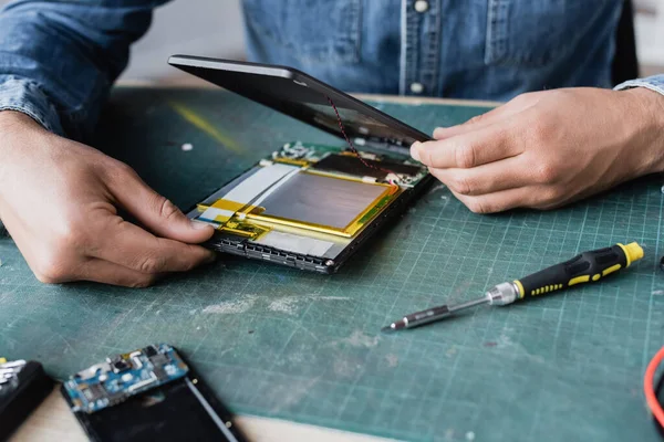 Vue rapprochée des mains de réparateur démonter une tablette numérique cassée près d'un tournevis sur le lieu de travail — Photo de stock