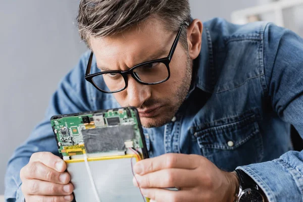 Focused repairman in eyeglasses looking at part of broken digital tablet — Stock Photo