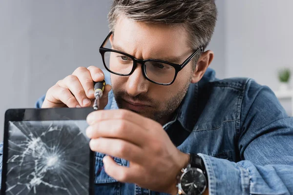 Focused repairman with screwdriver fixing smashed display of digital tablet on blurred foreground — Stock Photo