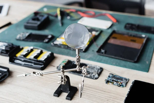 Flat lay of magnifier with disassembled parts of devices on workplace on blurred background — Stock Photo