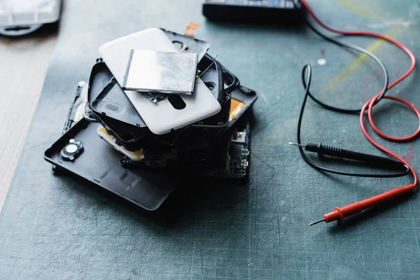 Vue rapprochée téléphones démontés pile près de multimètre sur le lieu de travail sur fond flou — Photo de stock