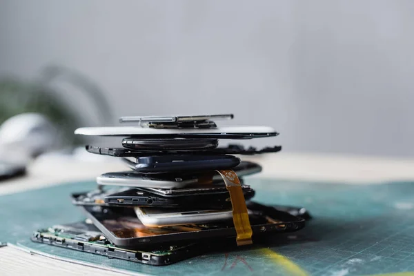 Vista de cerca de la pila con teléfonos móviles desmontados y baterías con lugar de trabajo borroso en el fondo - foto de stock