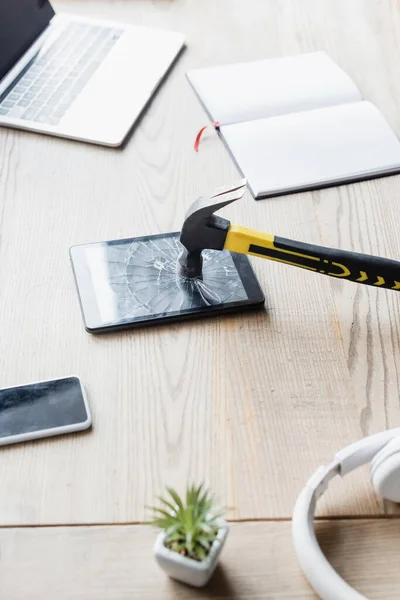 Hammer on smashed digital tablet near headphones and blank notebook on table with digital devices — Stock Photo