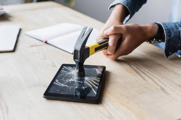 Vue recadrée de l'homme d'affaires frappant tablette numérique avec marteau sur le lieu de travail sur fond flou — Photo de stock