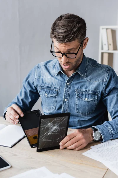 Surprised businessman disassembling smashed digital tablet at workplace on blurred foreground — Stock Photo