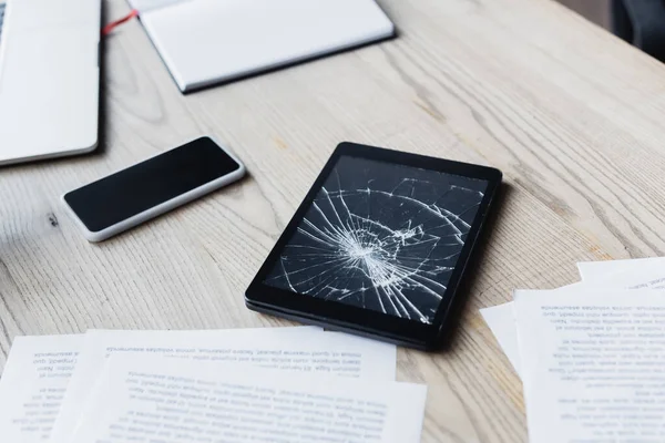 Tablet digital esmagado perto de documentos e dispositivos digitais em fundo de madeira — Fotografia de Stock
