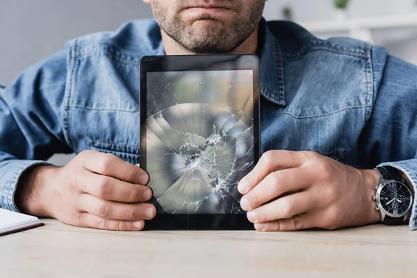 Cropped view of businessman holding smashed digital tablet on wooden table — Stock Photo