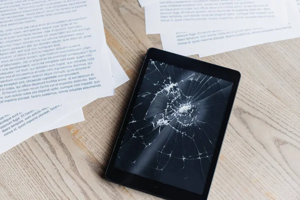 Top view of smashed digital tablet with documents on textured wooden background — Stock Photo