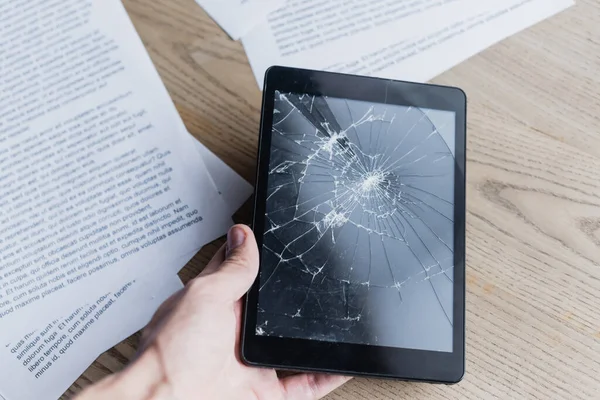 Vista recortada del hombre de negocios sosteniendo mesa digital aplastada cerca de documentos sobre fondo de madera - foto de stock