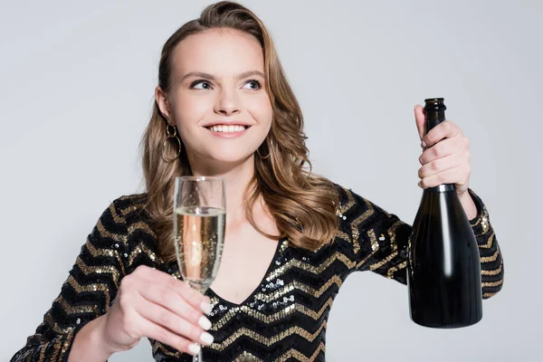 Mujer feliz sosteniendo copa de champán y botella aislada en gris - foto de stock