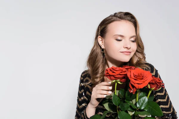 Feliz joven mujer oliendo ramo de rosas rojas aisladas en gris - foto de stock