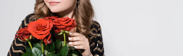 Vue recadrée d'une jeune femme heureuse sentant le bouquet de roses rouges isolées sur gris — Photo de stock