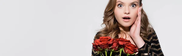 Impactada joven mujer sosteniendo ramo de rosas rojas aisladas en gris, bandera - foto de stock