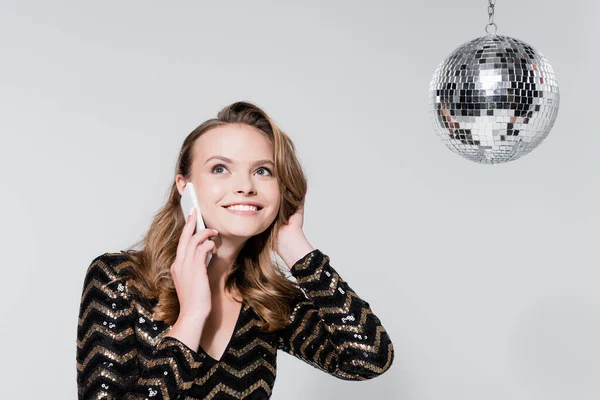 Весела молода жінка розмовляє на смартфоні біля диско-кулі ізольована на сірому — стокове фото