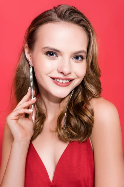 Cheerful young woman in earrings smiling on red — Stock Photo