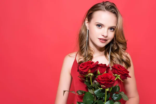 Alegre joven mujer sosteniendo rosas y mirando a la cámara en rojo - foto de stock