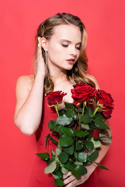 Молода жінка дивиться на троянди і фіксує волосся на червоному — стокове фото