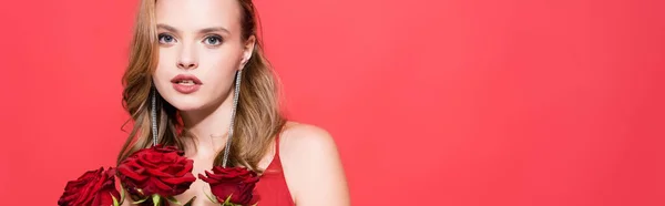 Young woman holding roses and looking at camera on red, banner — Stock Photo