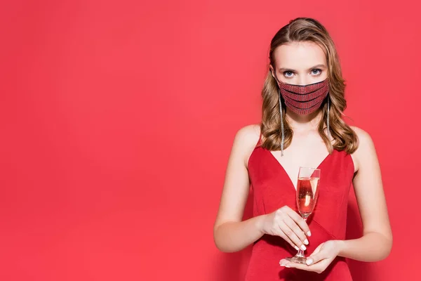Jovem mulher em máscara protetora com strass segurando vidro com champanhe em vermelho — Fotografia de Stock