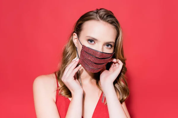 Jovem mulher usando máscara protetora com strass e olhando para a câmera no vermelho — Fotografia de Stock