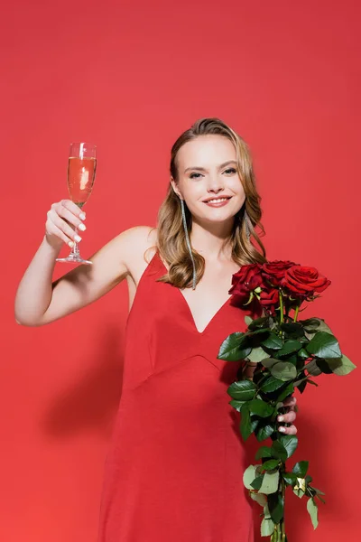 Freudige Frau mit Rosen und einem Glas Champagner auf Rot — Stockfoto