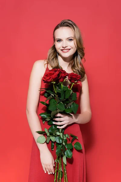 Feliz joven mujer mirando a la cámara y sosteniendo rosas en rojo - foto de stock