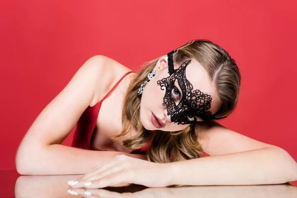 Jeune femme élégante en dentelle masque de carnaval regardant la caméra sur rouge — Photo de stock