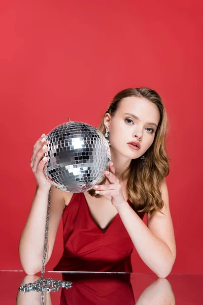 Jeune femme tenant brillant boule disco et regardant la caméra sur rouge — Photo de stock