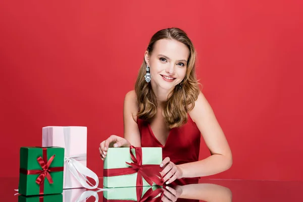 Щаслива молода жінка посміхається біля різдвяних подарунків на червоному — стокове фото