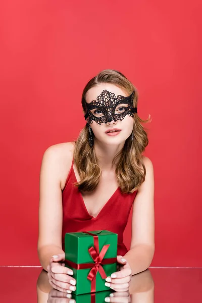 Mujer joven en elegante máscara de encaje celebración de Navidad presente en rojo - foto de stock