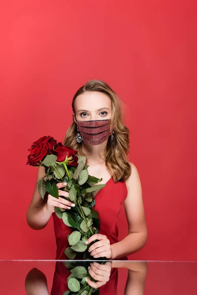 Donna in maschera protettiva con strass che regge rose su rosso — Foto stock