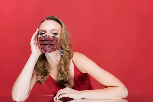 Jovem mulher em máscara protetora com strass olhando para a câmera no vermelho — Fotografia de Stock
